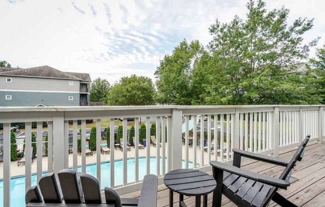 A wooden deck with a table and two chairs overlooking a pool.