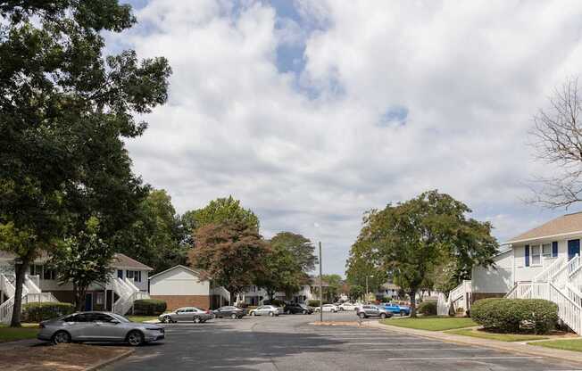 A residential street with houses on both sides and cars parked on the side.