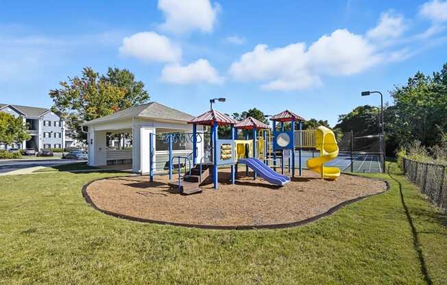 A playground with a yellow slide and a white building.