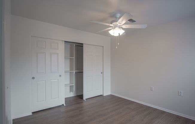 an empty bedroom with fan and closet