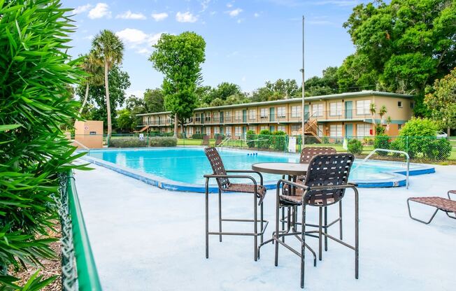 A poolside table with chairs is set up next to the Park Apartments swimming pool in Daytona Beach, FL.