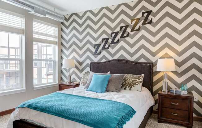 A bedroom with a bed, two lamps, and a wall with a zigzag pattern.