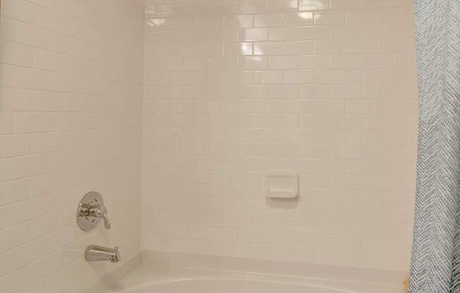 A white bathtub with a shower head and a blue shower curtain.
