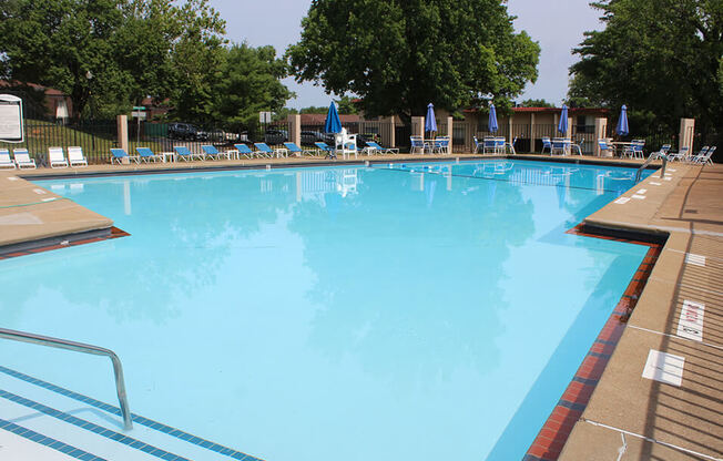 a large swimming pool with lounge chairs and trees in the background