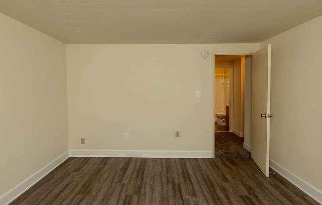 A room with a wooden floor and a doorway leading to another room.