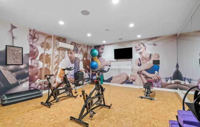 A gym with exercise bikes and a wall mural of people exercising.