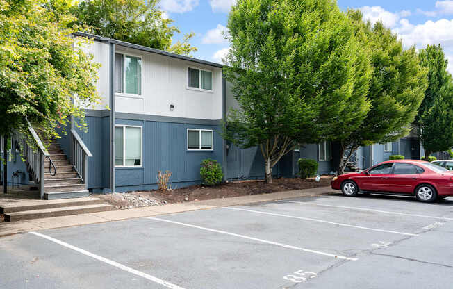 A red car is parked in a parking lot in front of a two-story building.
