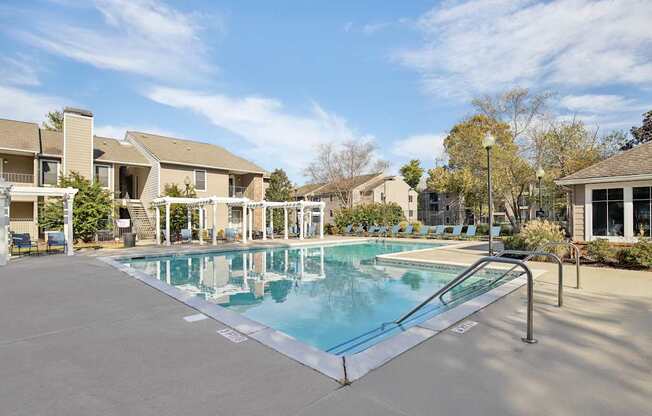 A swimming pool surrounded by a concrete floor and metal railings with a building in the background.
