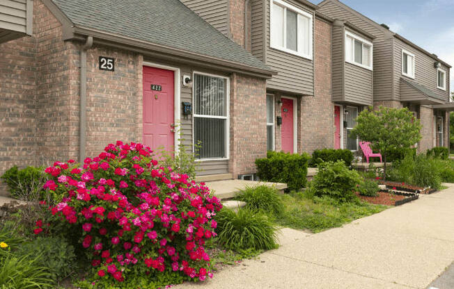 a pink door on a brick house with a pink flower bush in front of it