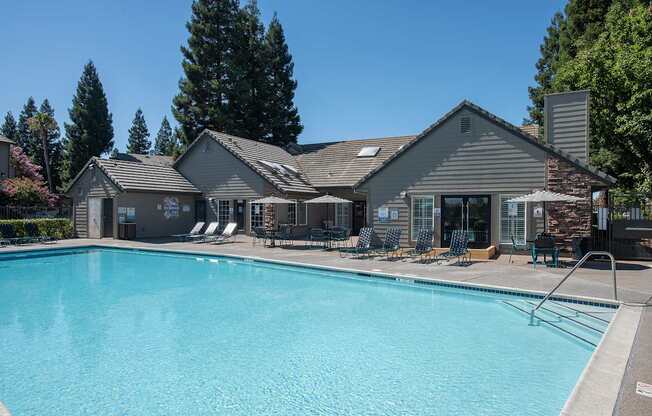 A large swimming pool in front of a clubhouse with a patio and lounge chairs at Sunset Summit, Rocklin, CA, 95765