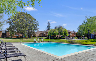 a swimming pool with chaise lounge chairs and trees in the background