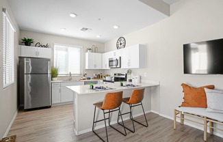 an open kitchen and living room with a white counter top and a stainless steel refrigerator