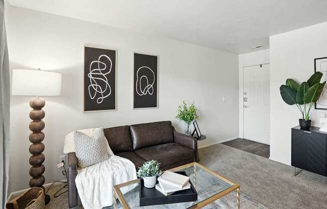 A living room with a brown couch, a glass coffee table, and two abstract art pieces on the wall.