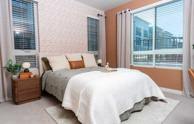 A bedroom with a bed, nightstand, and window with blinds.