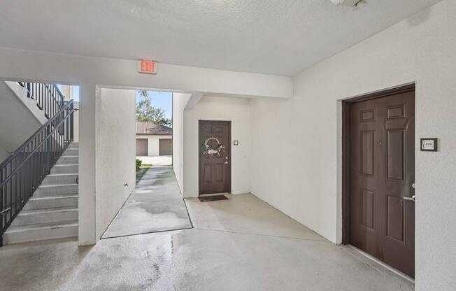 A hallway with a brown door and a red exit sign above it.