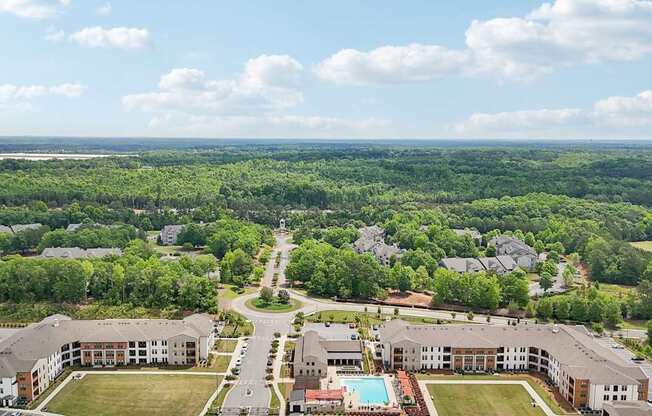 aerial view of the apartment complex with the pool ad many trees in view with beautiful skies