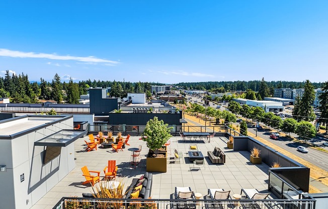 A rooftop patio with orange chairs and tables overlooks a cityscape.