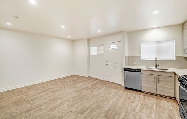 the living room and kitchen of an apartment with a wooden floor and white walls