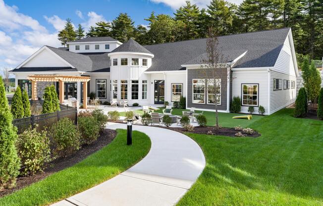 A winding walkway leads to the bright and welcoming clubhouse, complete with lounge seating, games, and inviting spaces to gather indoors and out.