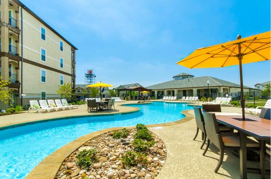A pool area with chairs and umbrellas is surrounded by a stone border.
