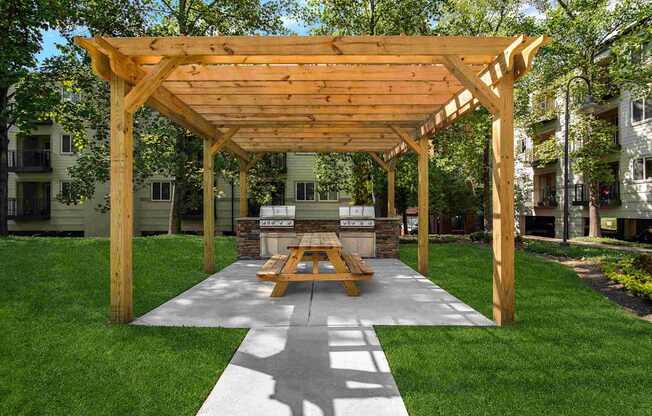 A wooden pavilion with a picnic table in the middle of a grassy area.