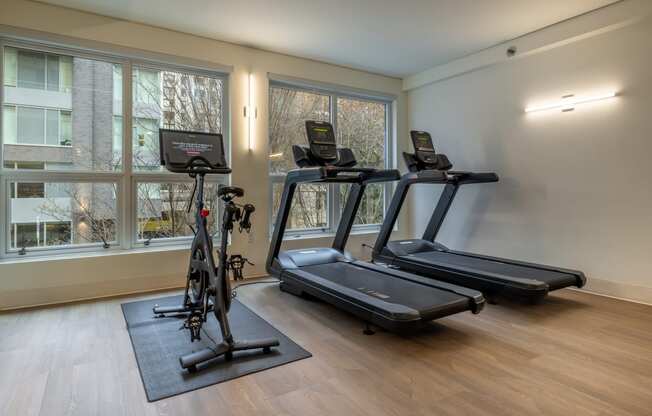 two treadmills and a bike in a room with windows