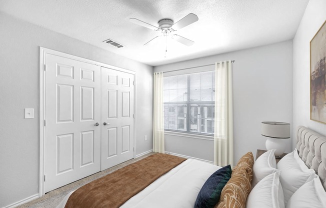 A bedroom with a bed, a ceiling fan, and a window with curtains.