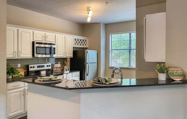 A kitchen with a black granite counter top and white cabinets in the 1486 square foot 3 bedroom, 3 bath apartment with attached 2-car garage at The Brownstones in Far North, Dallas, Texas