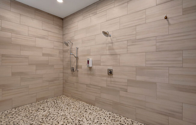 A clean spa shower room here at The Park featuring modern tiled walls, pebble-style flooring, dual showerheads, and a bright, refreshing design that creates a comfortable and inviting wellness space.