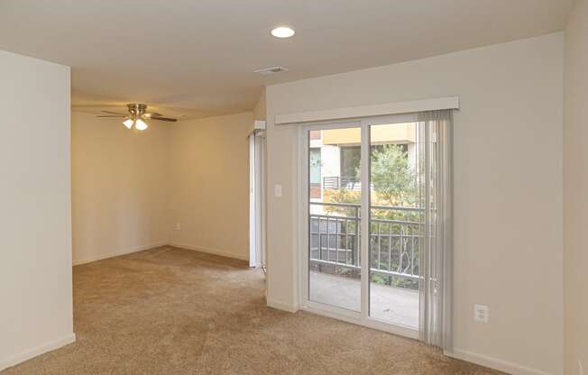 an empty living room with a large window and a ceiling fan