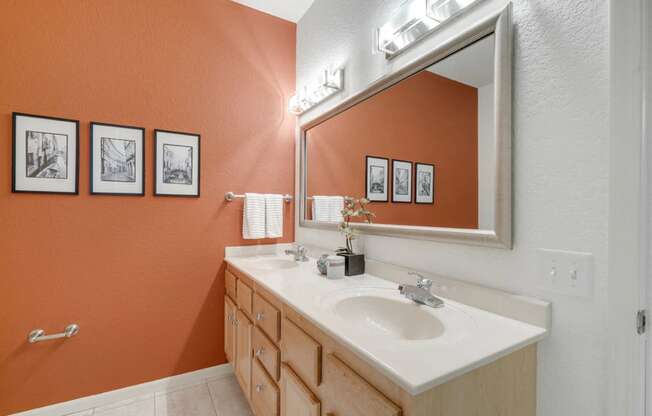 Bathroom with twin sinks and an orange wall with artwork