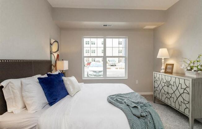 A bedroom with a large bed, a nightstand, and a window with a view of the street.