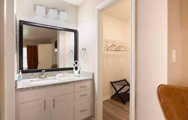 A bathroom with a mirror, a white cabinet, and a brown chair.