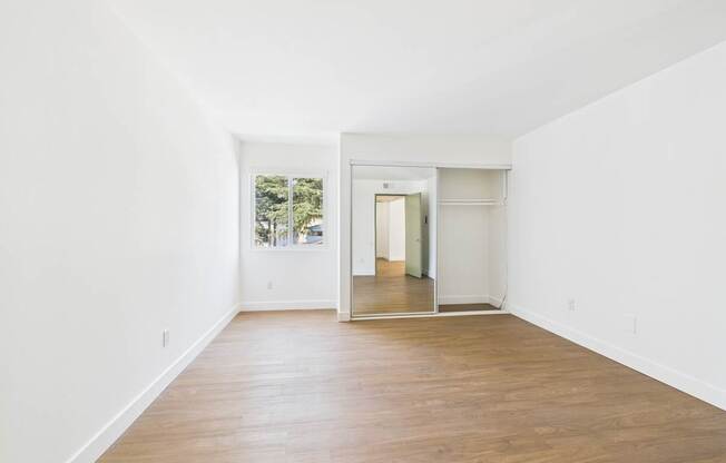 A room with white walls and wooden flooring with a doorway leading to another room.