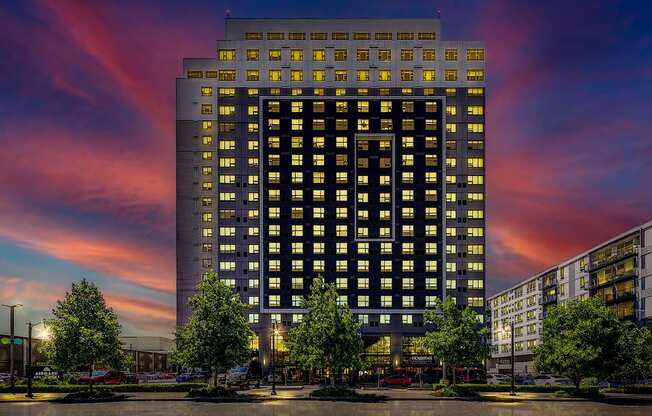 A tall building with many windows is lit up at dusk.