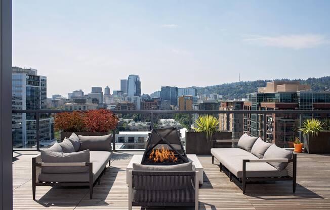 a roof deck with chairs and a fire pit overlooking a city