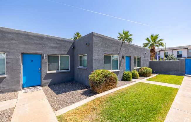 a gray house with blue doors and a lawn