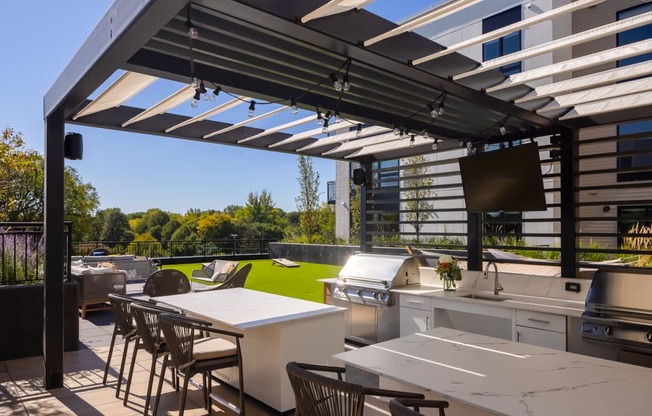 a pergola with white tables and chairs on a patio with a grill and a television
