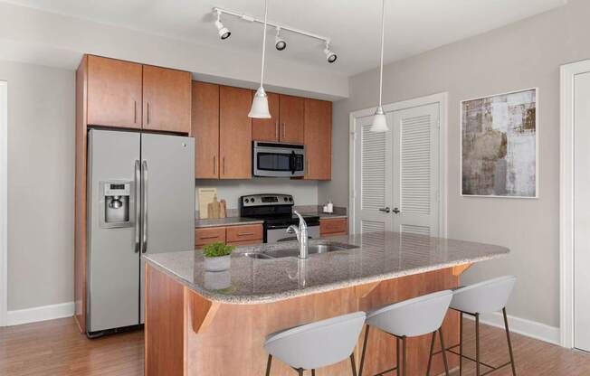A kitchen with a refrigerator, microwave, oven, sink, and bar stools.