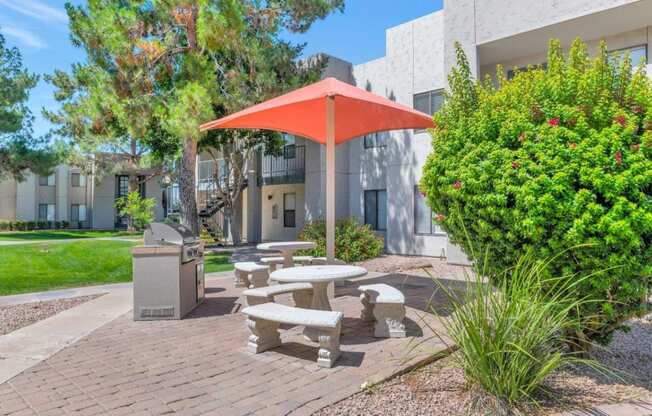 a picnic table with a red umbrella in front of a building