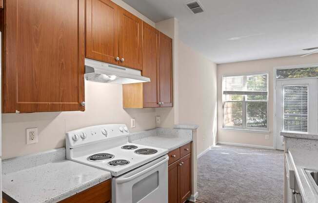 The kitchen of Ten05 West Trade Apartments, featuring a refrigerator and a white stove. The room is lit by the oven's overhead light and plenty of natural light from large windows.