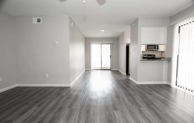 an empty living room with wood floors and a kitchen