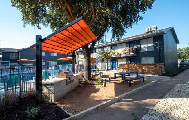 Poolside patio at Studio 700 apartments in Arlington, Texas with picnic table and grill with large prepping stations under an oak tree and large shade.