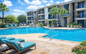 A pool surrounded by lounge chairs and palm trees.
