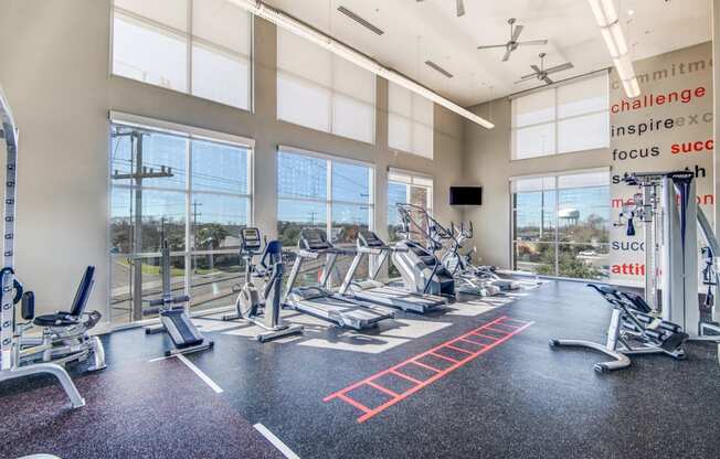 a gym with cardio machines and windows with a view of the city
