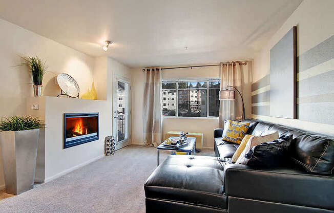 A black leather couch sits in a living room with a fireplace and a plant on the side table. at Mill Creek Meadows Apartments, Mill Creek, Washington