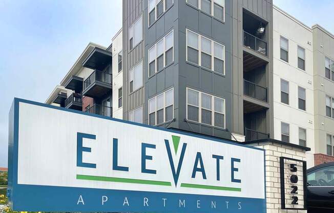 A sign for Elevate Apartments is in front of a building.