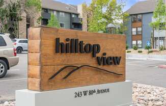 A wooden sign for Hilltop View sits in front of a parking lot.