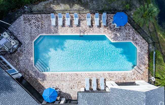 A rectangular pool surrounded by a brick patio and lounge chairs.