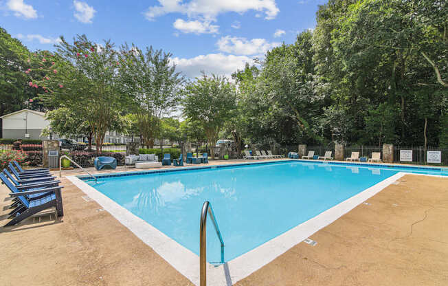 A large outdoor swimming pool surrounded by trees and lounge chairs.